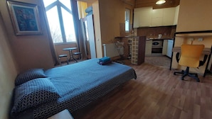 A compact room with a bed, a desk, and a kitchenette.