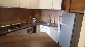 A kitchen with a gas stove, a sink, a kettle, and a refrigerator.