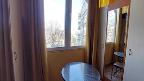 A small room with a single round glass table, a window, and a mirror reflecting the room.