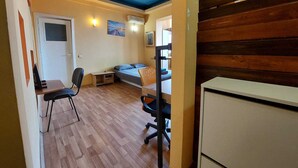 A compact room with a bed, a desk, a chair, and a small table.