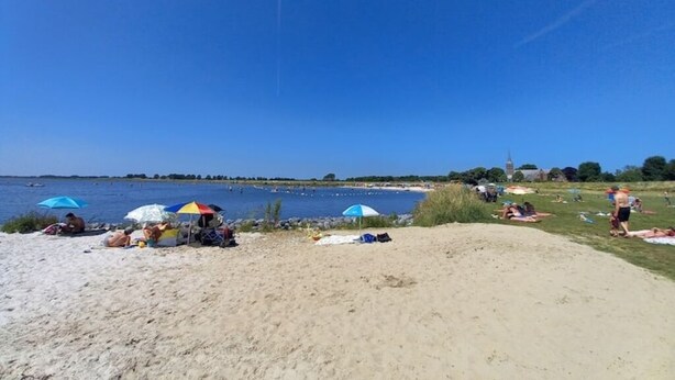 A beach with people sunbathing and swimming, umbrellas, and a clear blue sky.
