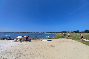 A beach with people sunbathing and swimming, umbrellas, and a clear blue sky.