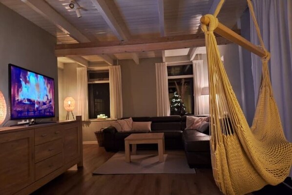 A cozy living room with a sofa, a coffee table, a TV, and a hammock.
