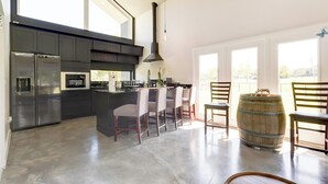 A modern kitchen with dark cabinetry, stainless steel appliances, a central island with bar stools, and a large wooden barrel.