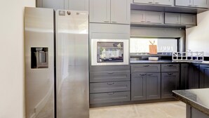 A modern kitchen with grey cabinets, a stainless steel refrigerator, and a built-in oven.