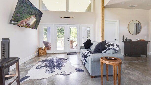 A spacious living room with a large TV mounted on the wall, a sofa with patterned cushions, a coffee table, and a large rug.