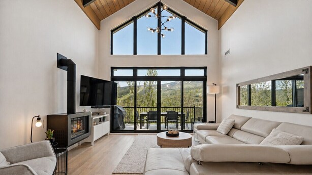 A spacious living room with a fireplace, a television, a sofa, and a balcony with a view.