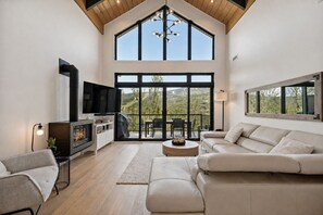 Ein geräumiges Wohnzimmer mit Kamin, Fernseher, Sofa und einem Balkon mit Blick.