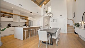 A modern kitchen with white cabinetry, a central island with bar stools, and a dining area with a large table and chairs.