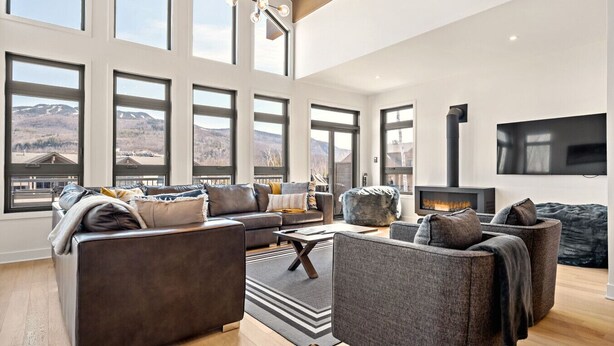 Un salón amplio con ventanas grandes, una chimenea y un televisor de pantalla plana.