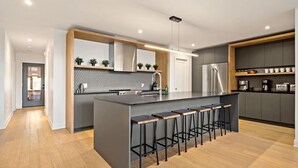 Una cocina moderna con una isla central, taburetes de bar, electrodomésticos de acero inoxidable y un salpicadero hexagonal.