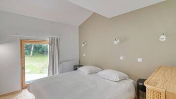 Een slaapkamer met een bed, een houten nachtkastje, een kleine tafel en een raam met gordijnen.