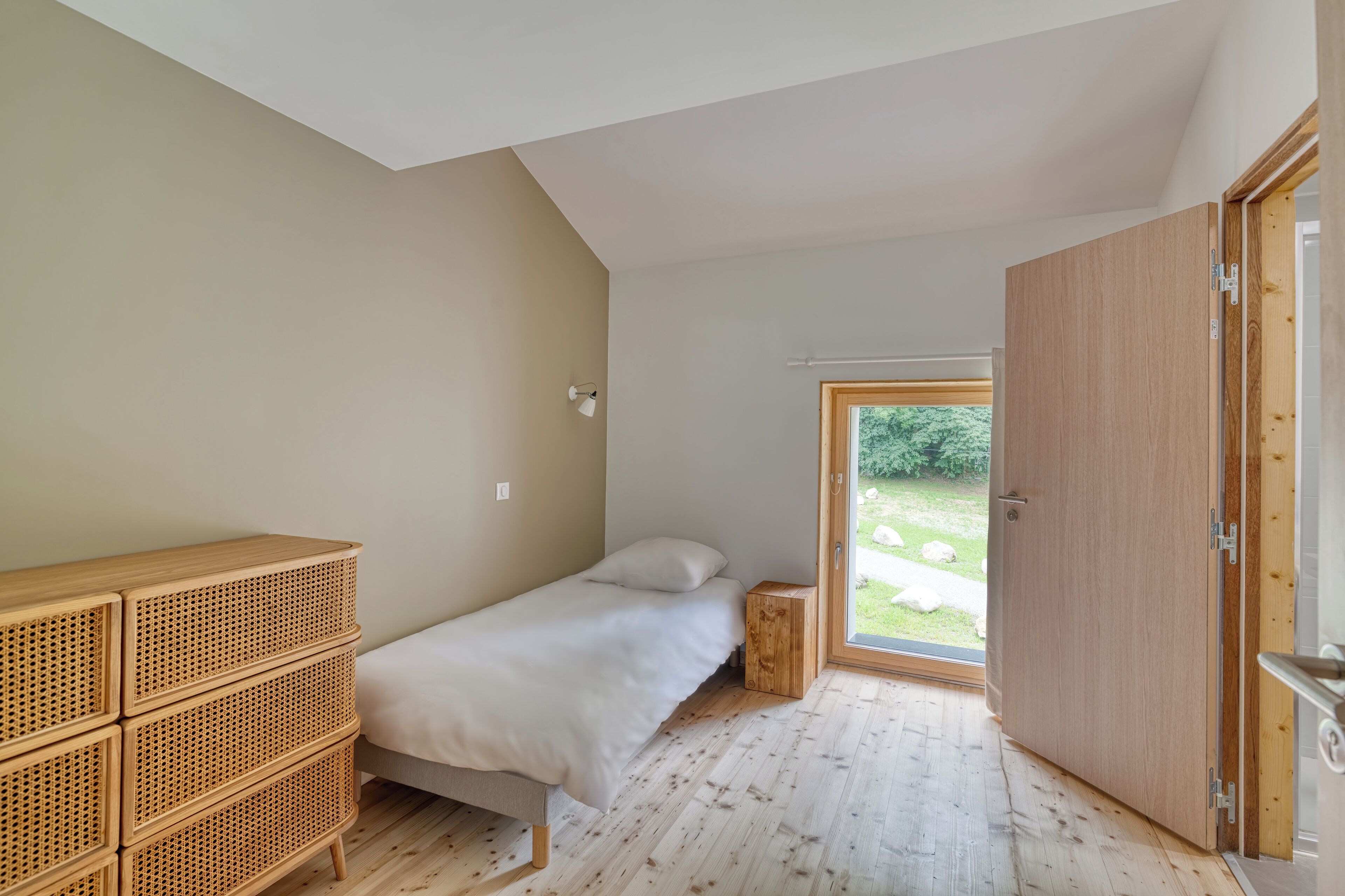 Ein Schlafzimmer mit einem Einzelbett, einem Holzschrank und einer Schiebetür, die auf einen Balkon führt.