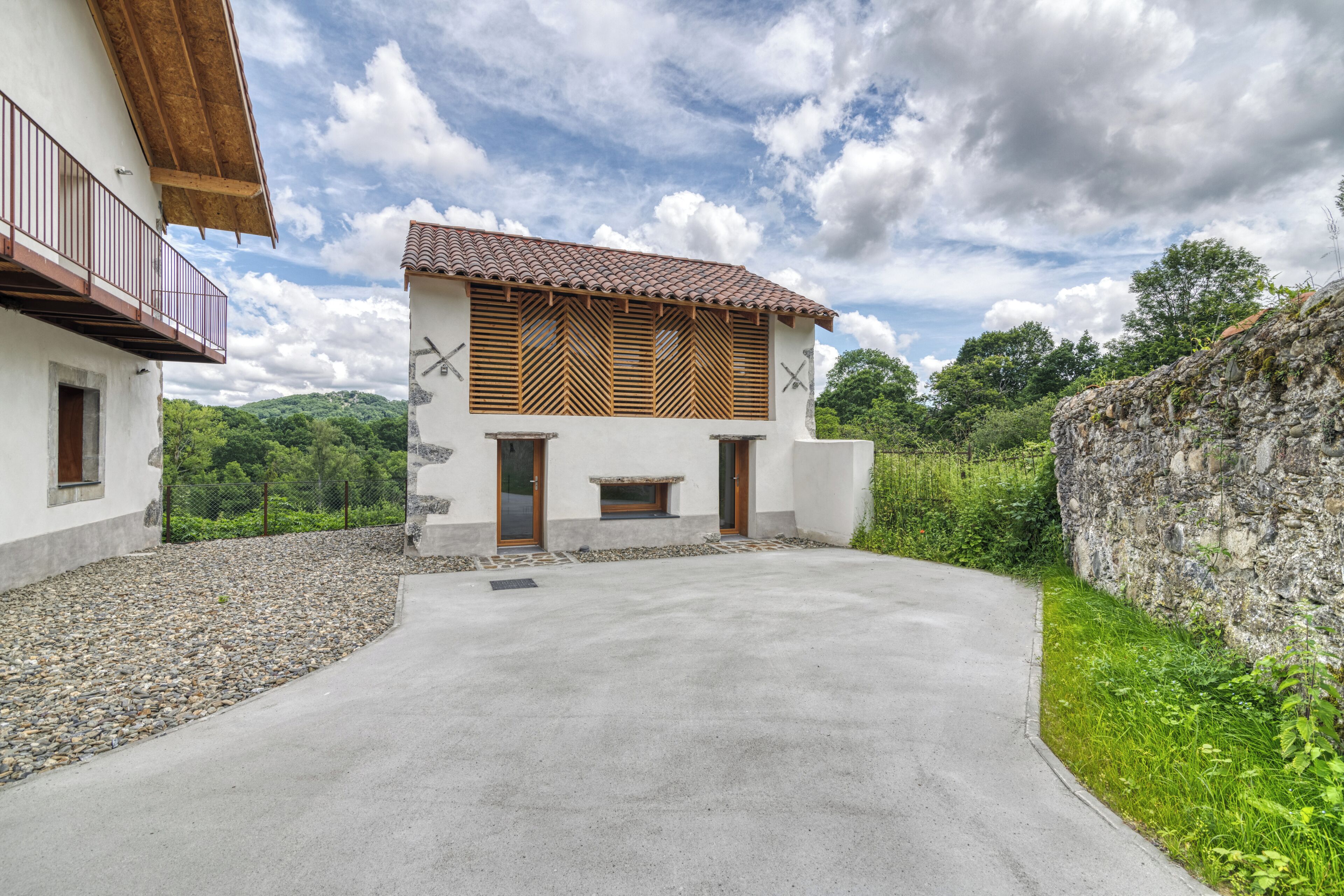 Un bâtiment moderne avec une allée en béton, des fenêtres à persiennes en bois et un mur en pierre.