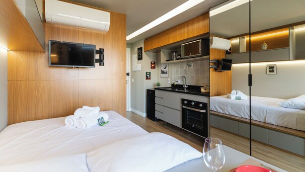 A hotel room with a bed, a TV, a kitchen area, and a mirror. - Legacy Klabin (Sao Paulo)