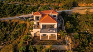 A large, two-story house with a red-tiled roof, surrounded by dense greenery and a paved driveway. - Sea Whisper Villa Peloponnese (North Kynouria)