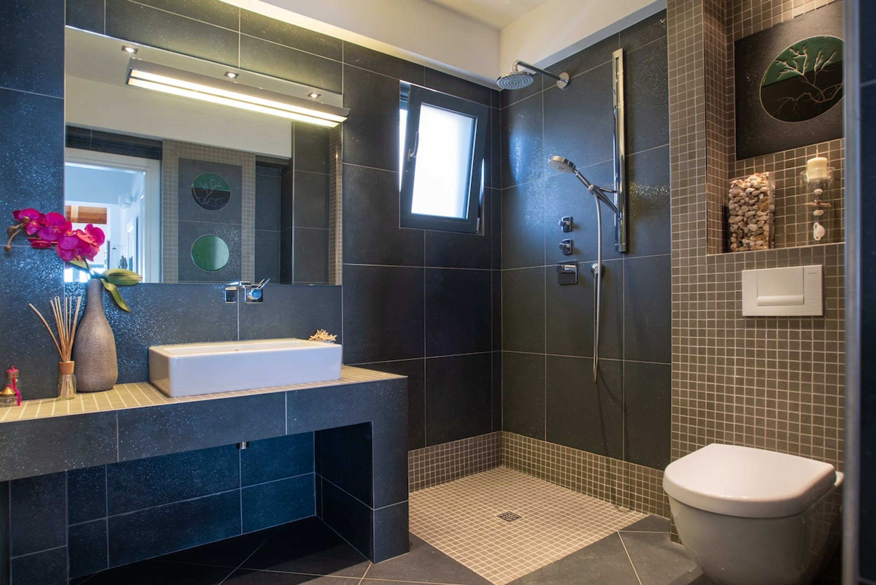 A modern bathroom with a large mirror, a white sink, a shower area, and a toilet.
