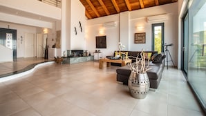 A spacious living area with a high ceiling, a fireplace, a sofa, and a large window. - Sea Whisper Villa Peloponnese (North Kynouria)