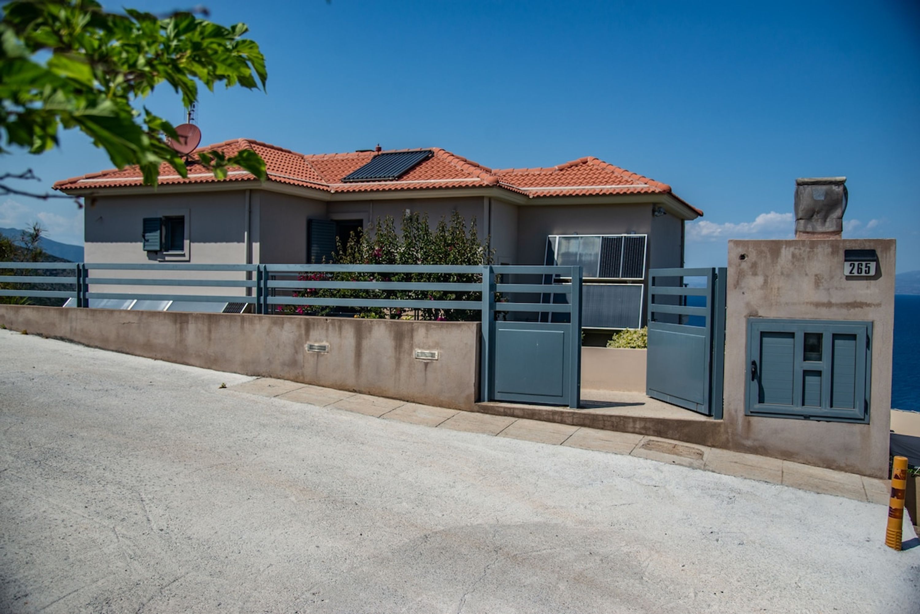 A two-story house with a red-tiled roof, a satellite dish, and a gated entrance.