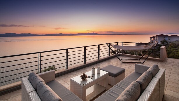A terrace with a view of the sea at sunset, featuring a sofa set, a table, and a hammock. - Sea Whisper Villa Peloponnese (North Kynouria)