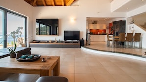 A modern living room with a wooden ceiling, a large TV, and a dining area with a table and chairs. - Sea Whisper Villa Peloponnese (North Kynouria)
