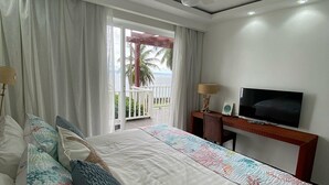 A hotel room with a bed, a TV, a desk, and a balcony with a view of the ocean.