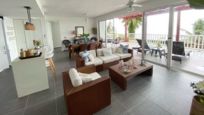 A spacious living area with a dining table, sofa, and chairs, a ceiling fan, and a view of the outdoors.