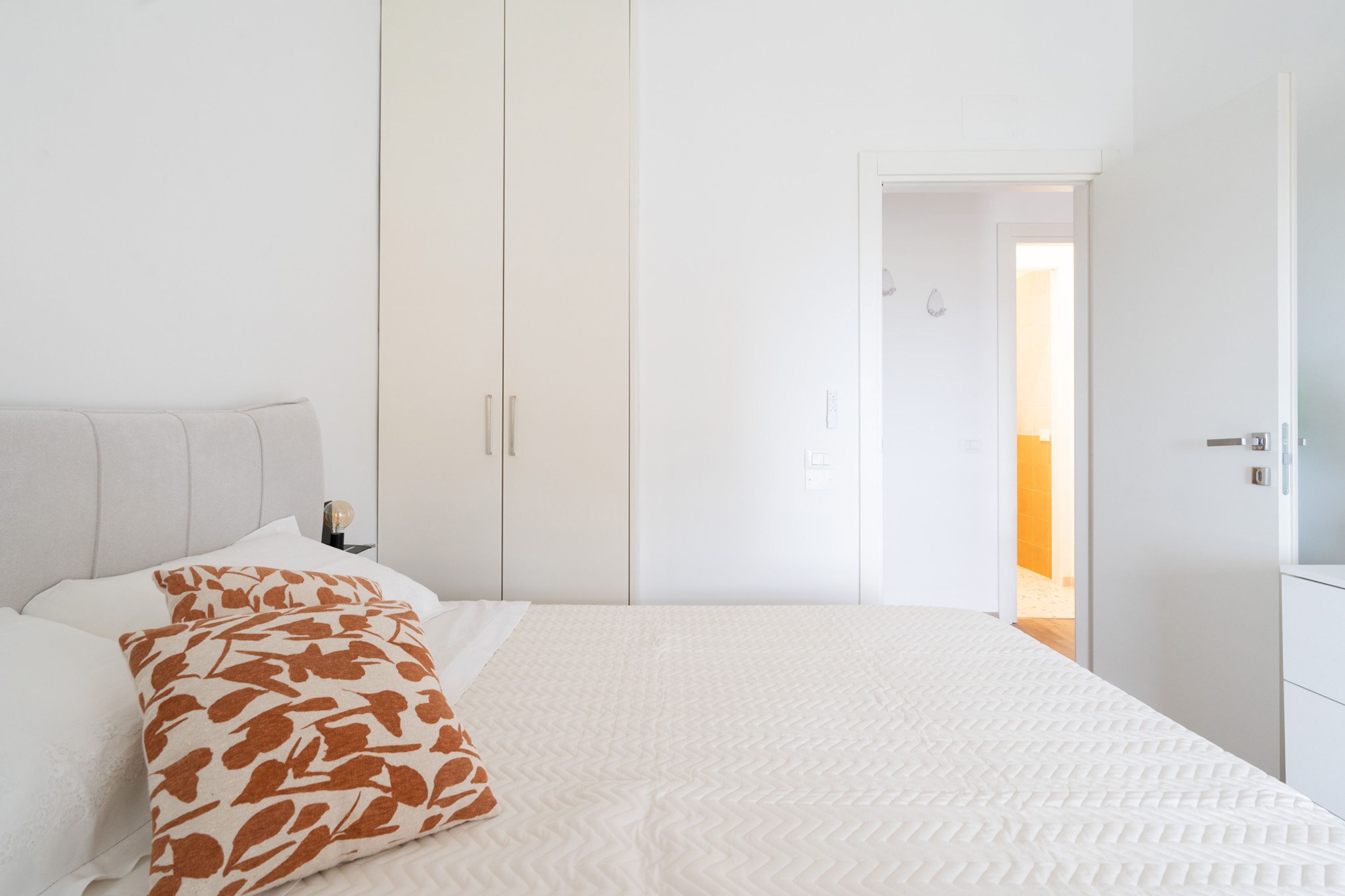 Un dormitorio con cama, armario blanco y mesita de noche con lámpara.