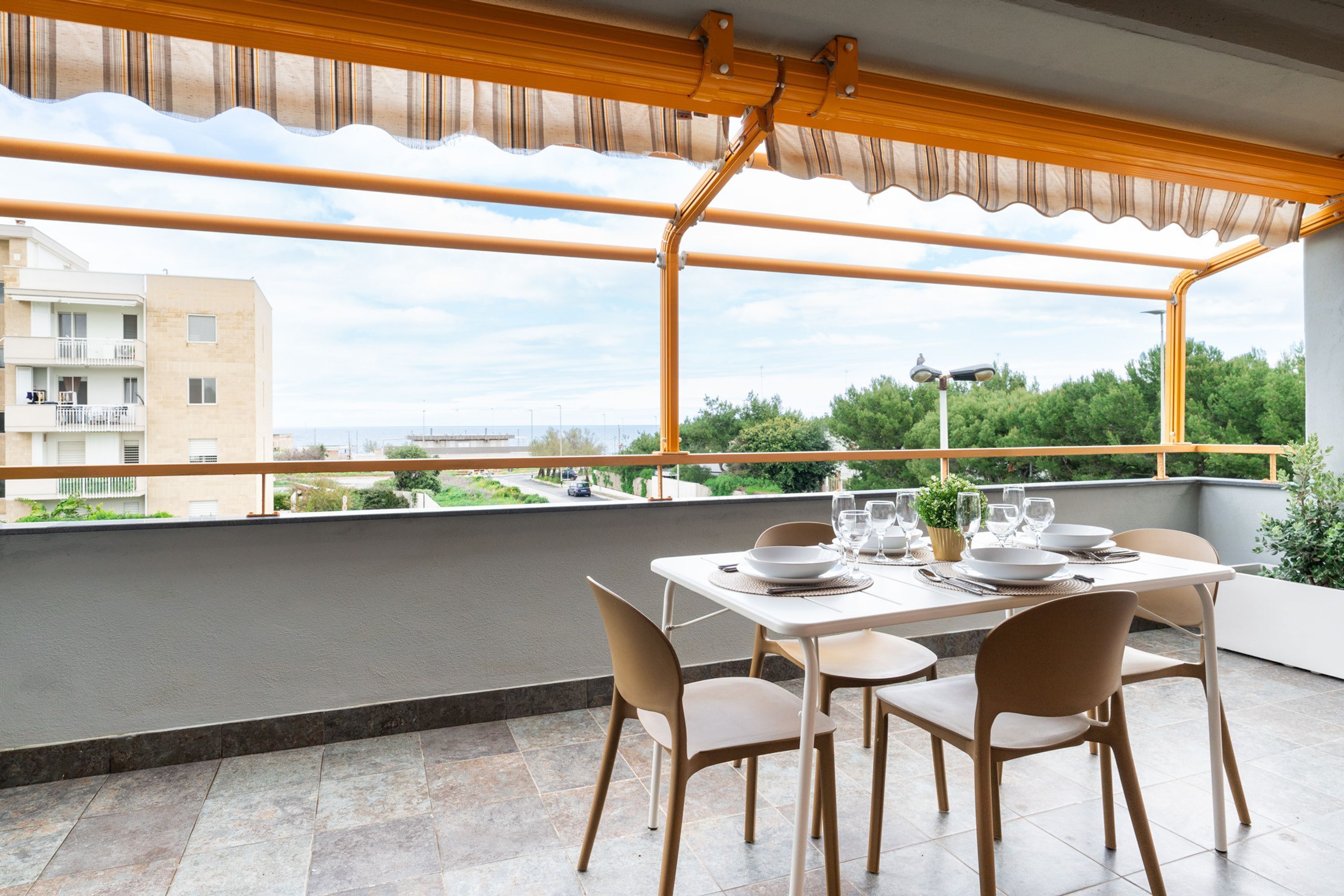 Un balcon avec une table dressée pour le repas, des chaises et une vue sur la mer et les bâtiments.