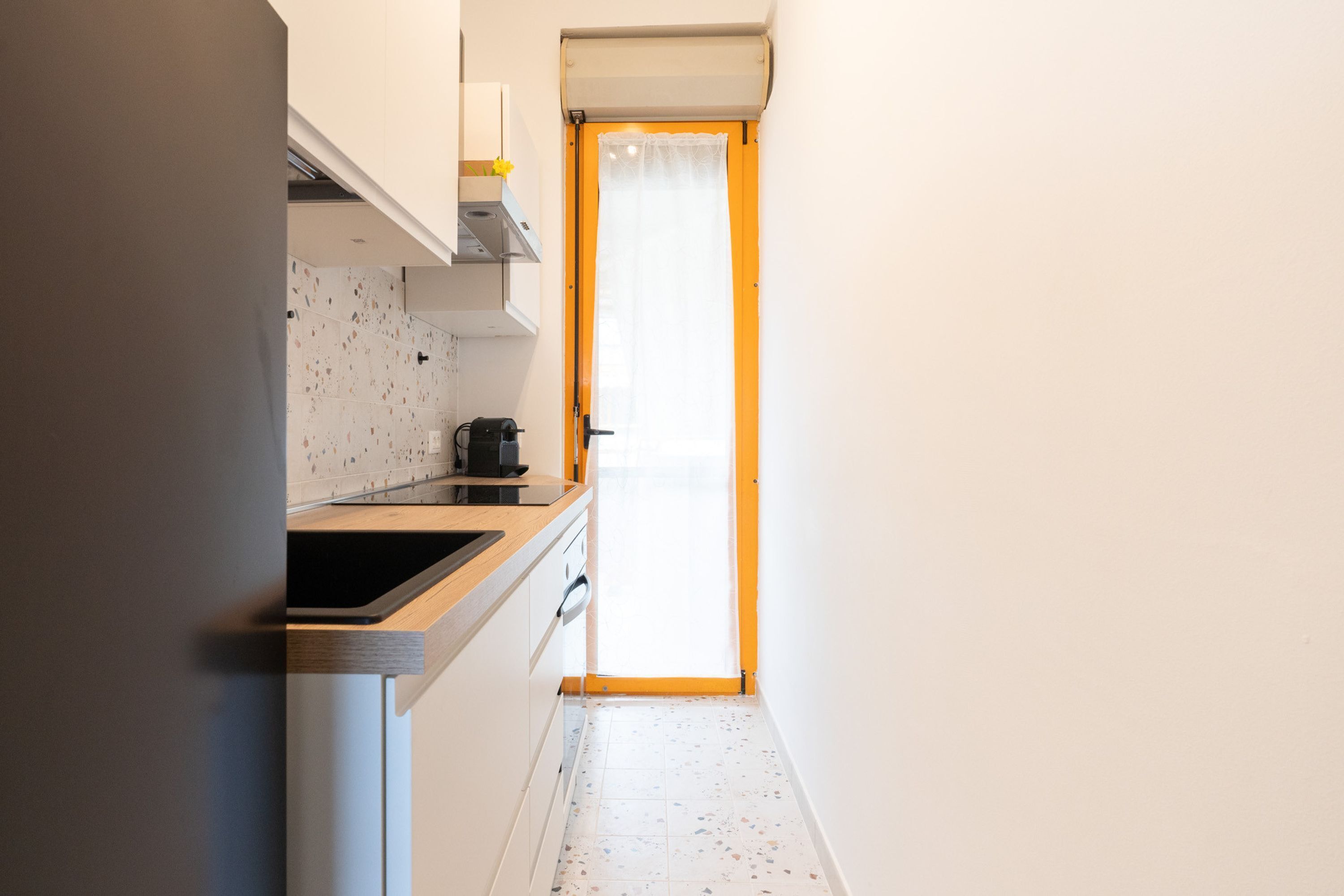 Una cocina estrecha con paredes blancas, una encimera de madera y un ventanal con una puerta amarilla.