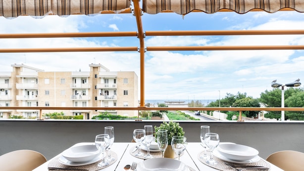 A balcony table set with white plates, glasses, and cutlery, overlooking a residential area with buildings and greenery. - Casa Levante by Wonderful Italy (Bari)