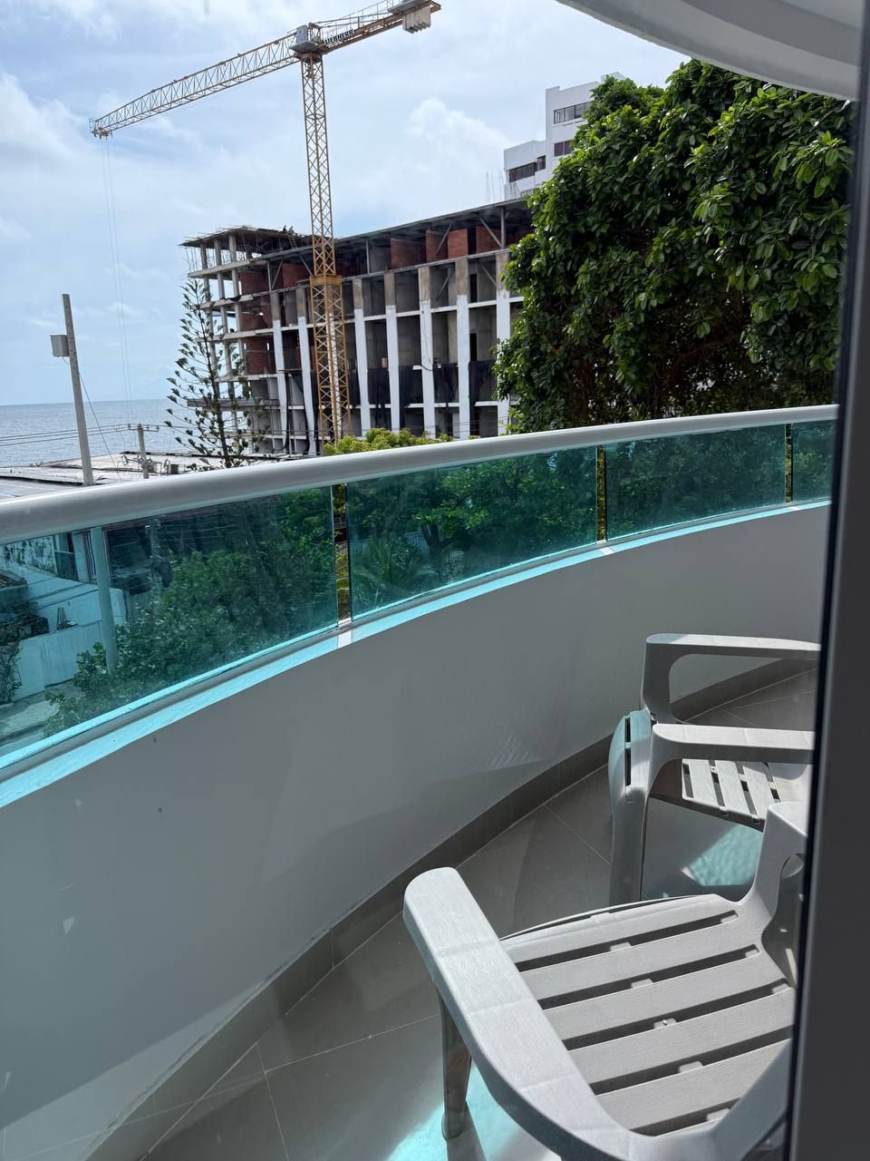 A balcony with a glass barrier, a white chair, and a table.