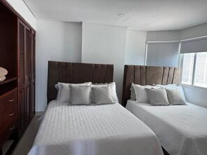 Ett hotellrum med två sängar, en garderob i trä och ett fönster med persienner.