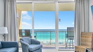 A hotel room with a balcony overlooking a beach, featuring a sofa, a chair, and a TV stand. - Majestic Beach Towers 1-503 (Panama City Beach)