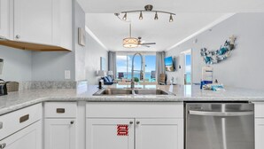 A modern kitchen with a stainless steel dishwasher, a sink, and a fire extinguisher sign on the cabinets. - Majestic Beach Towers 1-503 (Panama City Beach)