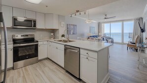 A modern kitchen with a built-in oven, microwave, and dishwasher, a large island with a sink, and a dining area with a view of the ocean. - Majestic Beach Towers 1-503 (Panama City Beach)
