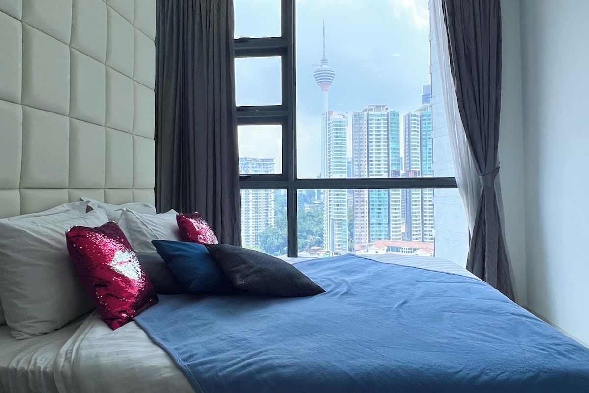 A bedroom with a large window, a bed with blue bedding, and a view of a cityscape including a tower.