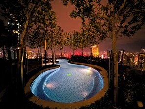 A nighttime swimming pool with a cityscape view, surrounded by trees and illuminated by artificial lighting. - The Robertson Residence KL (Kuala Lumpur)