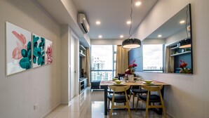 A modern dining area with a table, chairs, and a pendant light. There are wall-mounted air conditioning units and a large window with a view of buildings.