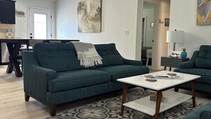 Una sala de estar con un sofá verde, una mesa de centro blanca y un tapete estampado.