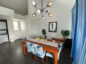 Un coin repas avec une table en bois, des chaises, un lustre et des plantes en pot.