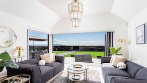 A modern living room with a large window, two sofas, a coffee table, and a chandelier. - No.36 South Beach - Donnini Apartments  (Troon)