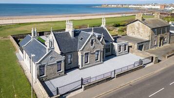 Traditional coastal property with a steeply pitched roof and multiple chimneys, situated adjacent to a sandy beach.