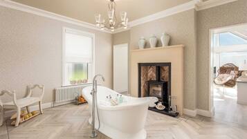 A spacious bathroom with a freestanding bathtub, a fireplace, and a large window providing natural light.