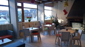 Enjoy dining in this warm and inviting space with a stone fireplace, wooden tables, and comfortable seating options.