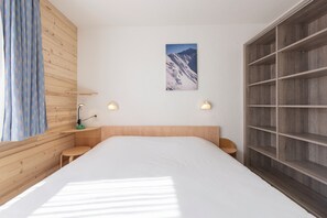 Un dormitorio con cabecera de madera, una cama grande, dos mesitas de noche, un estante en la pared y una imagen con vistas a la montaña.