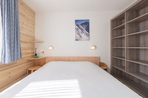Un dormitorio con cabecera de madera, una cama grande, dos mesitas de noche, un estante en la pared y una imagen con vistas a la montaña.