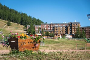 A wooden planter with flowers labeled "LES KARELL" in a grassy area with a view of multi-story buildings in the background. - Vacances Bleues Arc En Ciel Les Karellis (Montricher-Albanne)