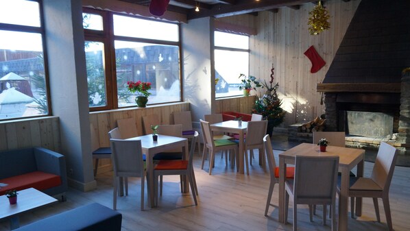 Un restaurante acogedor con paredes de madera y ventanas amplias, que cuenta con una chimenea y decoración festiva.