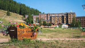 A wooden planter with flowers labeled "LES KARELL" in a grassy area with a view of multi-story buildings in the background. - Vacances Bleues Arc En Ciel Les Karellis (Montricher-Albanne)